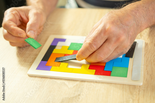 Photography senior man's engaged hands skillfully maneuver colorful wooden pieces brain teas