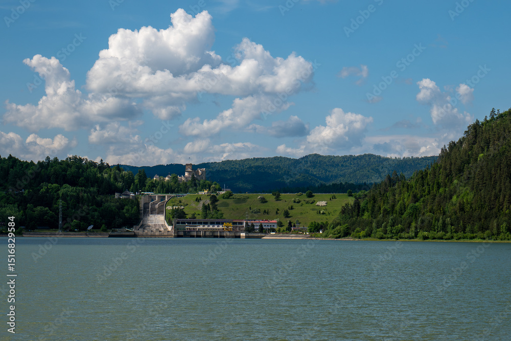 Fototapeta premium Hydroelectric dam and power station near Niedzica Castle in southern Poland, surrounded by forested hills and a lake on a sunny day.