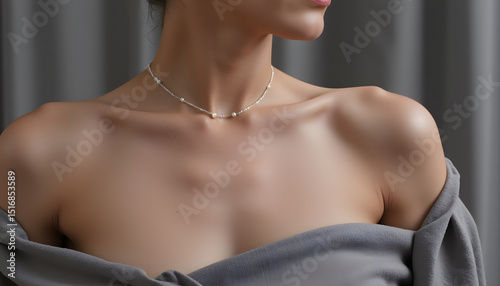 Woman showcasing delicate necklace while wearing gray off-shoulder top   photo