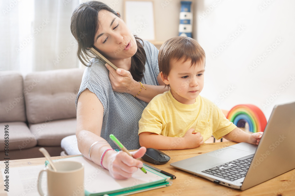 Mother taking notes while on phone and holding toddler during remote work Mother taking notes while on phone and holding toddler during remote work