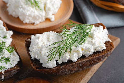 Home made rye bread on a wooden cutting board with curd cheese, ricotta and dill