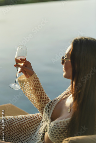 A 20s brunette woman holds a champagne flute at poolside in this elegant close-up shot, exuding sophistication