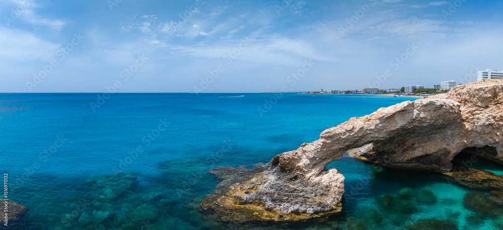 Fototapeta premium Coastal view in Ayia Napa, Cyprus, with a natural rock Love arch over clear turquoise waters, sandy beaches, and luxury resorts along the shoreline.