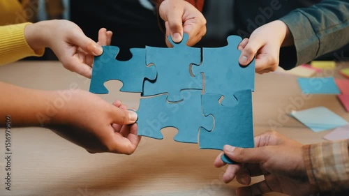 A close-up of hands from diverse business professionals working together with colorful puzzle pieces during a collaborative meeting in an office. SACTR
