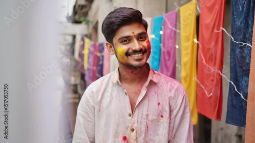 Wallpaper Mural Young man celebrating holi festival, smiling and looking away, with colorful powder on his face and clothes, standing in front of colorful fabrics hanging in the background Torontodigital.ca