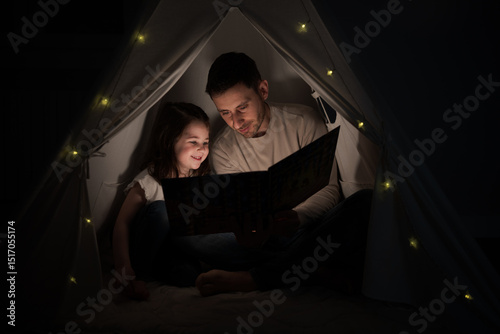 Father reading a bedtime story to his daughter in a blanket fort