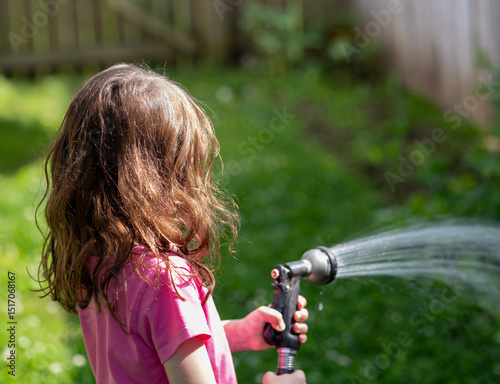 Little toddler girl watering the plants in the backyard in suburban