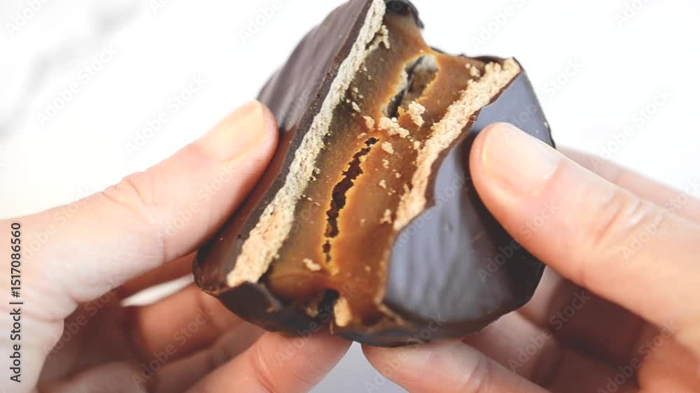 Female hands breaking a chocolate alfajor filled with dulce de leche.