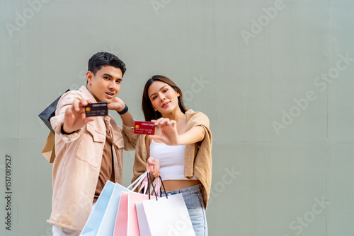 Happy Asian family enjoy urban lifestyle using credit card shopping black friday at department store. Portrait of Couple holding shopping bag and credit card at shopping mall on holiday vacation.