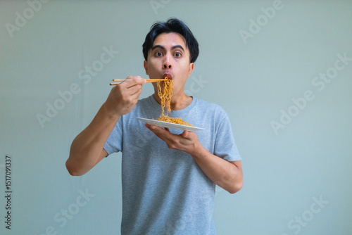 Happy young Asian man enjoying a plate of noodles with a cheerful expression, isolated on a clear background, perfect for food, lifestyle, or Southeast Asian culture themes