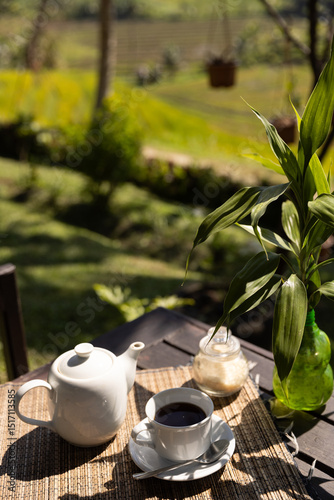 Balinese black tea with sugar served with a teapot at a picnic table overlooking a rice field on a sunny afternoon. photo