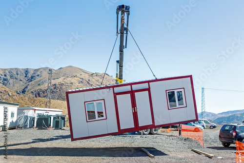 Crane lifts single storey prefabricated house. Prefabricated homes, often referred to as prefab homes or simply prefabs, are specialist dwelling types of prefabricated building, which are manufactured photo