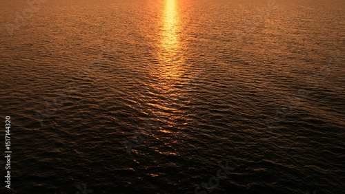 Aerial perspective reveals the shimmering, rippling surface of the sea, illuminated by the setting sun, with the light streaking across the water like liquid gold.
