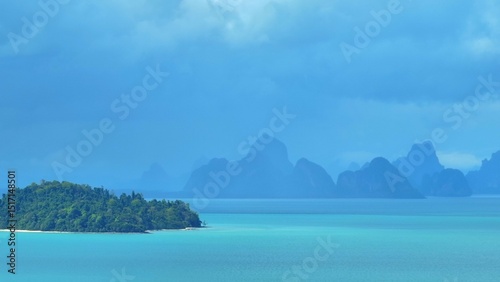 A dramatic aerial view of mountains in the distance, covered in mist and rain clouds, with the turquoise ocean beneath, creating a stunning and atmospheric coastal storm scene. Phuket, Thailand.
