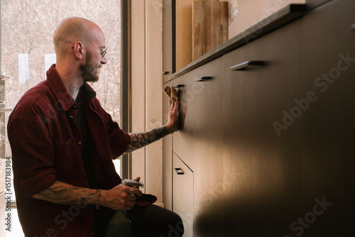 Man cleaning modern kitchen cabinets at home