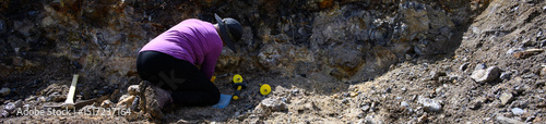 Mature woman rockhounding in Central Oregon, thunderegg pit with tools for digging, recreational hobby hunting for pretty rocks, sledgehammer, gloves, hammer, and pick
