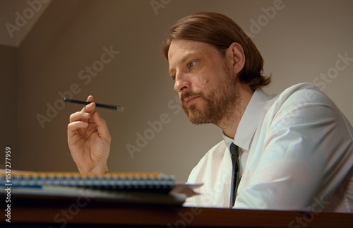 Pensive office worker concentrating on work, holding pencil photo