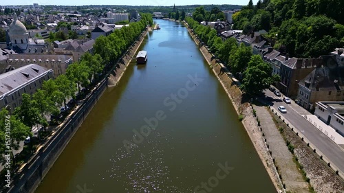 Drone flight over Laval reveals the Mayenne River, riverside trees, city center, and Saint-Julien Chapel in sunlight. France photo
