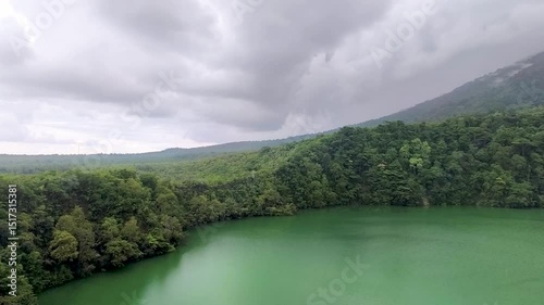 Aerial view of  Lake Tolire in Ternate, Indonesia, with vibrant green water surrounded by lush forest.
