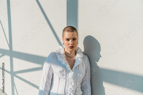 Person in white ruffled shirt leaning against sunlit wall