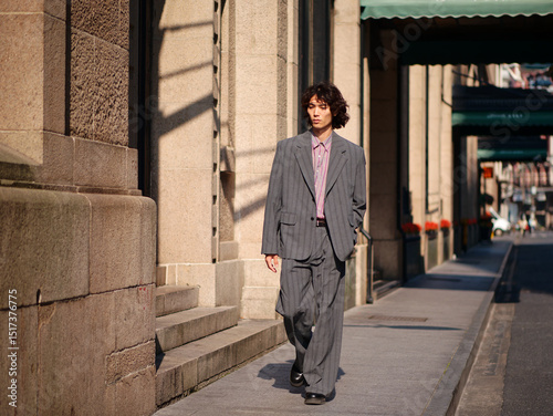 Portrait of handsome Chinese young man wearing gray suit walking in the street, young guy with black curly hair with urban background. Male fashion, cool Asian young man lifestyle.