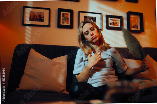 Woman Fanning herself with a Leaf at home during Summertime. Stressed unhappy lady feeling overheated at home 
