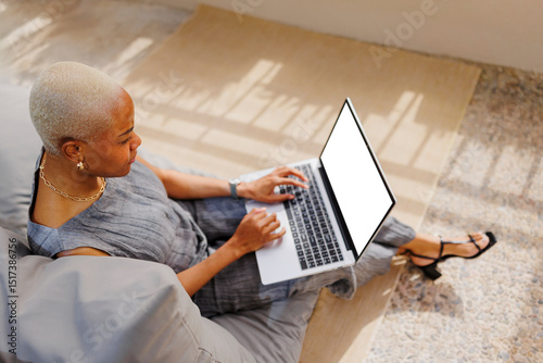 Female freelancer working on laptop in comfortable pouf on terrace