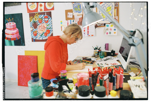 Artist working in colorful studio surrounded by paints and drawi