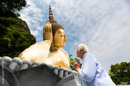 Elderly Thai woman praying to giant reclining Buddha statue at temple photo
