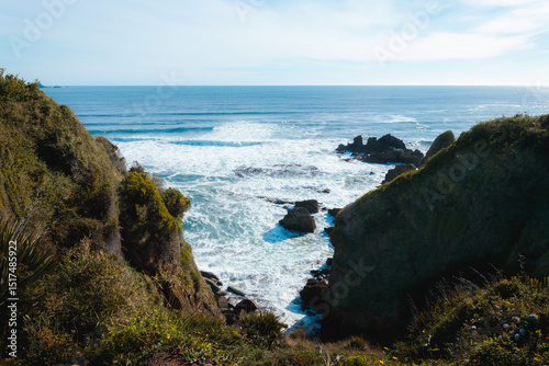 Ocean waves crashing on rocks between cliffs on sunny day photo