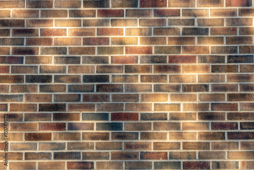 Abstract texture background of an exterior multi-shade reddish brown color vintage brick wall surface speckled with blue, in dappled sunlight from tree shadows