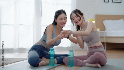 Two Asian women looking at smartwatches to measure their physical fitness during a break from exercise, health and wellness concept, exercise	