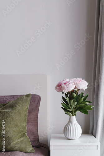 Simple Bedroom Interior Decor with Pastel Pink Peony Flowers in a White Ceramic Vase on a Bedside Table