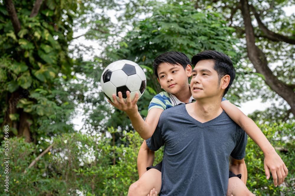 Obraz premium Father carrying son holding a ball on his back after playing soccer or football together in backyard