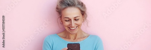 Attractive, aging female cheerfully using modern media device against a pastel pink wall indoors photo