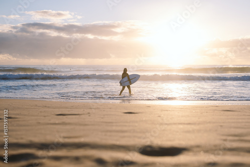 Surfer walking into ocean at sunrise on sandy manly beach