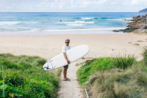 Surfer walking from beach towards ocean with surfboard under arm photo