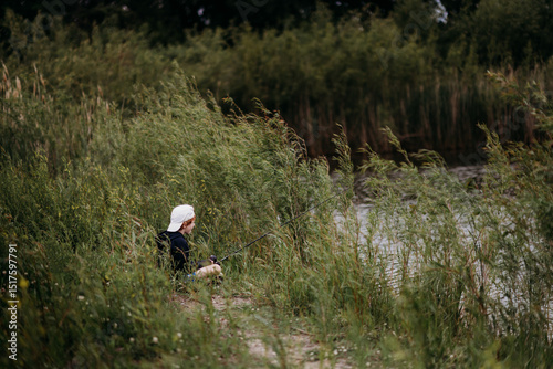 Young boy quietly fishing alone by overgrown riverbank reeds photo