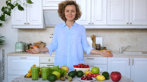 Enthusiastic nutritionist presenting a variety of fresh fruits, vegetables, and healthy green smoothies, promoting a balanced diet and healthy lifestyle in a modern kitchen setting