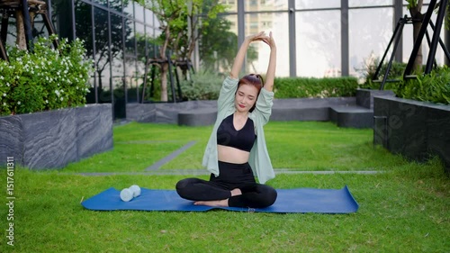 Engaging in a calming yoga session, Adult asian woman sitting on mat stretches her muscles and raises her hands towards the sky. Surrounded by greenery, she enjoys the serenity of her routine