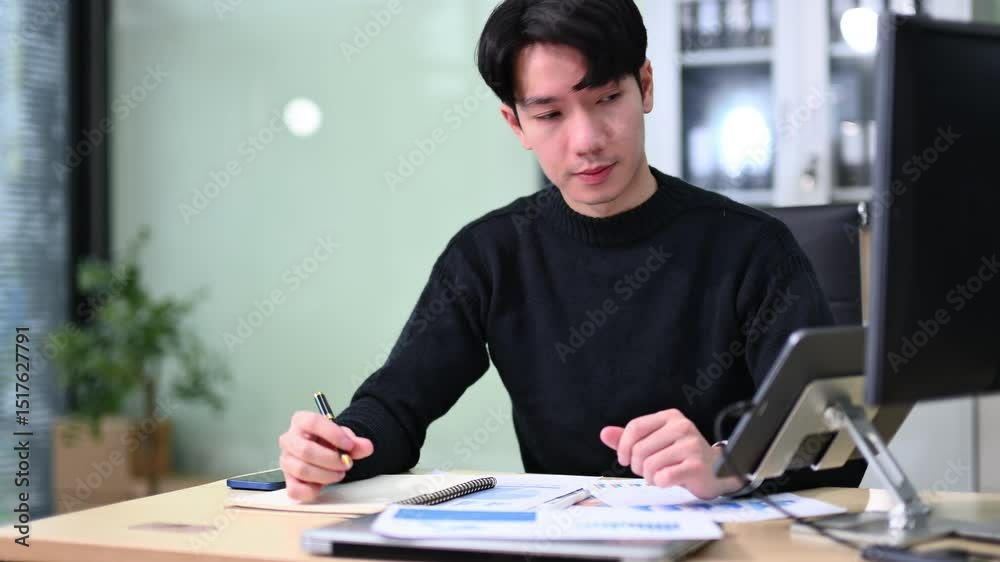 Asian man using laptop and tablet while sitting at her working place. Concentrated at work. Asian man using laptop and tablet while sitting at her working place. Concentrated at work.