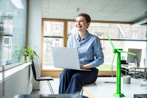 Smiling woman with laptop in modern office promoting sustainability