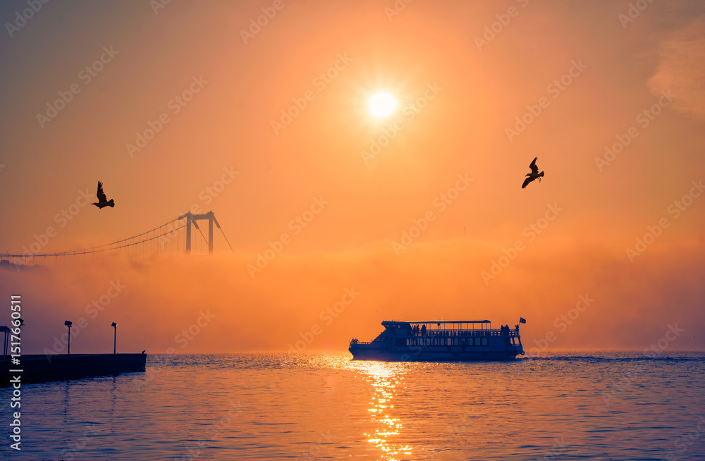 Fototapeta premium Ortakoy Mosque and Bosphorus Bridge in Istanbul, Turkey. Dramatic sky. The 15 July Martyrs Bridge in a fog. Passenger Boat on the Sea on a Foggy Day.