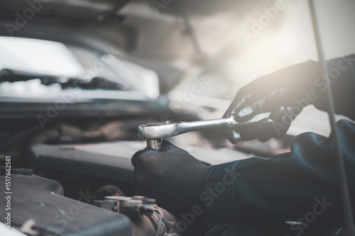 Close-up of professional car mechanic fixing a car. Mechanic is fixing the engine. Mechanic is wearing gloves and using a wrench.
