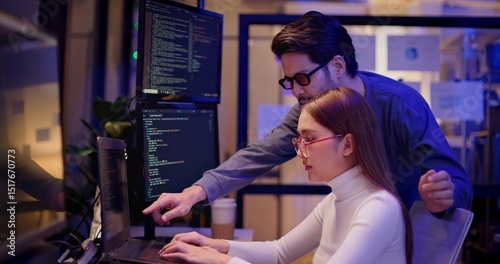 Two Asian software engineers collaborate at night in modern office, writing machine learning algorithms and debugging artificial intelligence code on multiple monitors in AI tech development workflow.