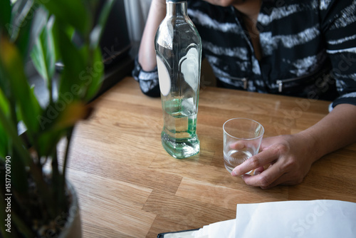 High angle view of hand of woman holding drinking glass with gin bottle at table