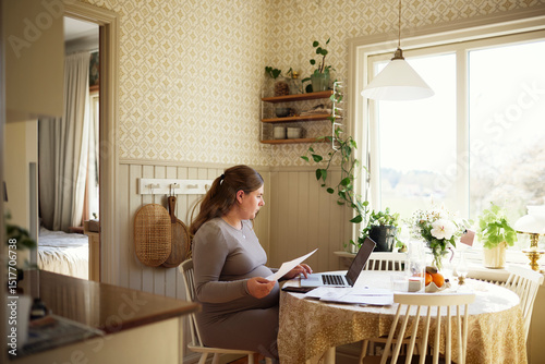 Wallpaper Mural Pregnant woman using laptop while calculating bills sitting at table in home Torontodigital.ca