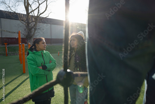 Female coach spending leisure time talking with teenage girl in jungle gym at sunny day