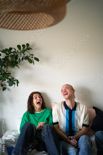 Carefree male and female friends enjoying with each other while sitting on bed at home