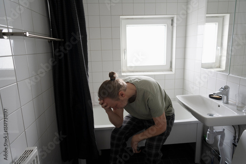 Depressed man sitting at edge of bathtub in bathroom